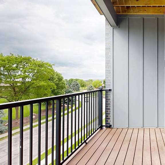 Thumbnail 70 of 84 Private apartment balcony with wood decking, black metal railing, and treetop views.