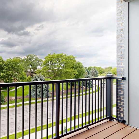 Thumbnail 69 of 84 Private apartment balcony with black metal railing and views of trees and neighboring homes under a cloudy sky.