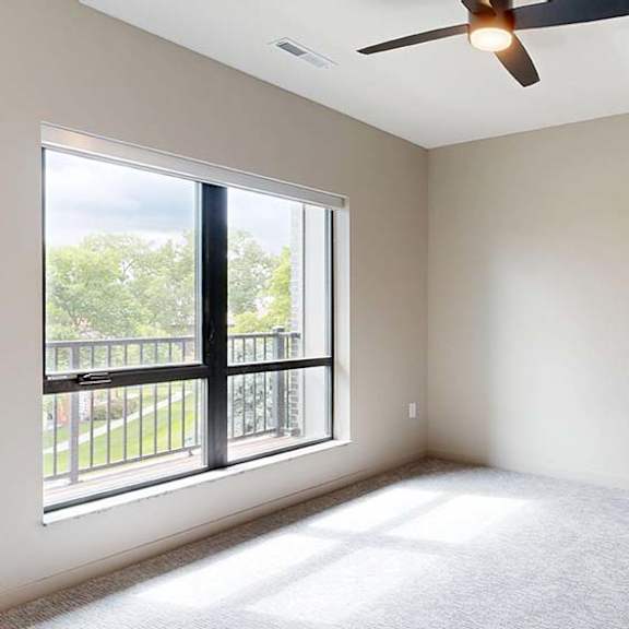 Thumbnail 65 of 84 A room with a ceiling fan and a large window overlooking a balcony.