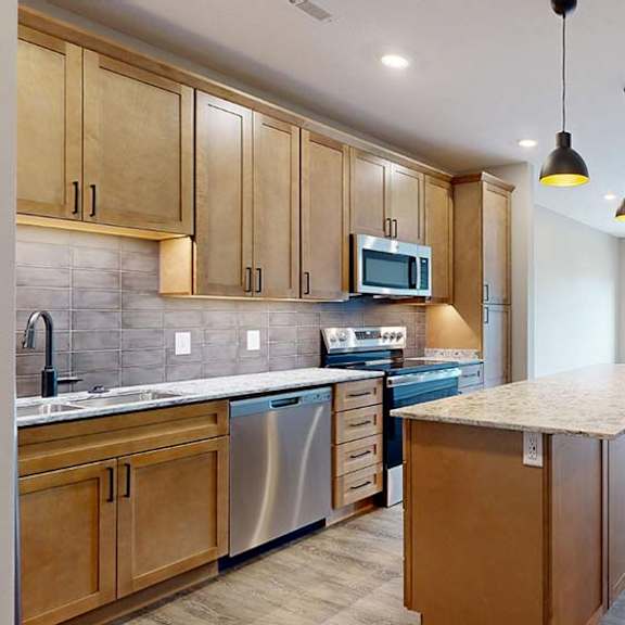 Thumbnail 53 of 84 Modern apartment kitchen with a large island, wood cabinetry, and stainless steel appliances.
