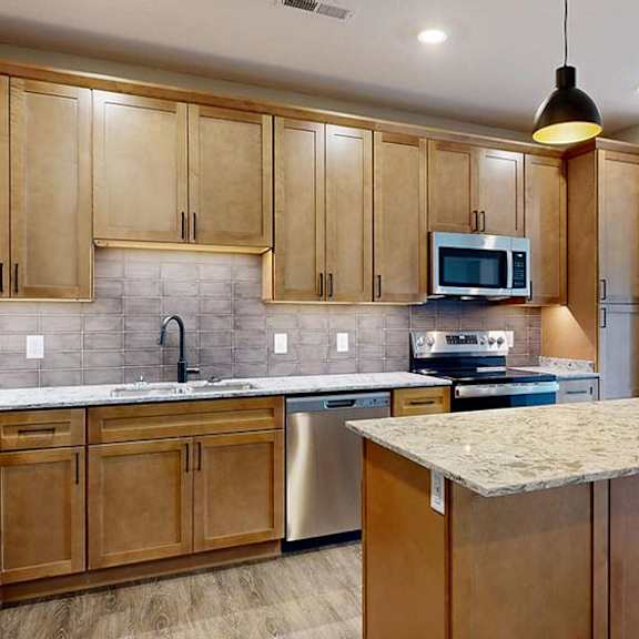 Thumbnail 55 of 84 Modern apartment kitchen with a large island, wood cabinetry, and stainless steel appliances.