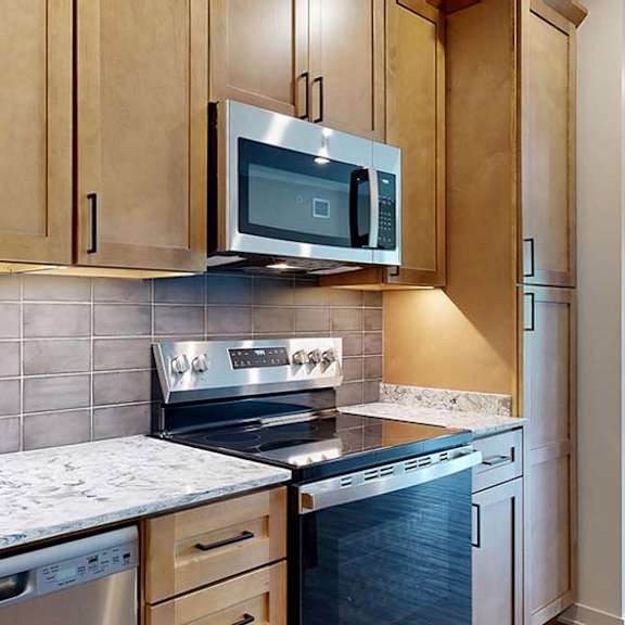 Thumbnail 56 of 84 Modern apartment kitchen with wood cabinetry, stainless steel appliances, and a tile backsplash.