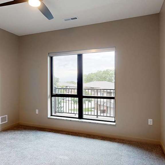 Thumbnail 48 of 84 Bright apartment bedroom with carpeted flooring, a large window, and a ceiling fan.