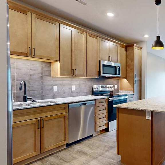 Thumbnail 39 of 84 Modern apartment kitchen with a large island, wood cabinetry, and stainless steel appliances.