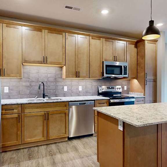 Thumbnail 41 of 84 Open-concept apartment kitchen featuring a center island, warm wood cabinets, stainless steel appliances, and pendant lighting overlooking the living area.