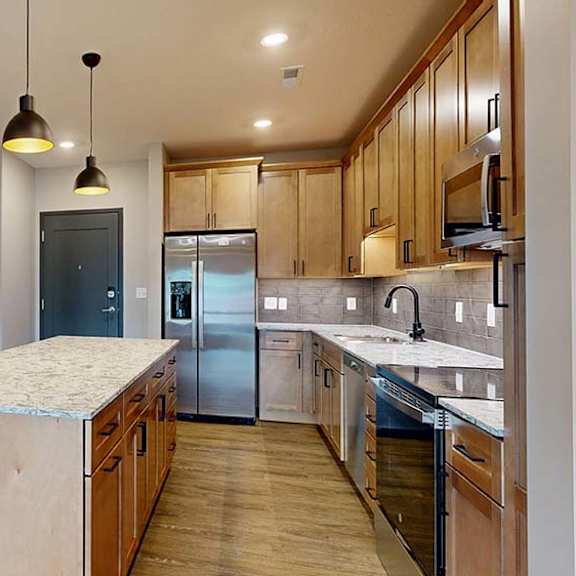 Thumbnail 42 of 84 Spacious apartment kitchen with an oversized island, tile backsplash, wood cabinetry, and stainless steel appliances in a bright open layout.