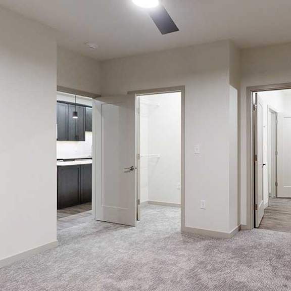 Thumbnail 76 of 84 Carpeted apartment bedroom with neutral walls, ceiling fan, and doorways leading to a bathroom and hallway.