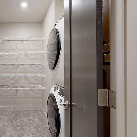 Thumbnail 31 of 36 Apartment laundry closet with a stacked washer and dryer and built-in wire shelving.