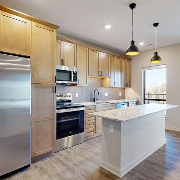 Thumbnail 23 of 36 Modern apartment kitchen with a large island, wood cabinetry, and stainless steel appliances.