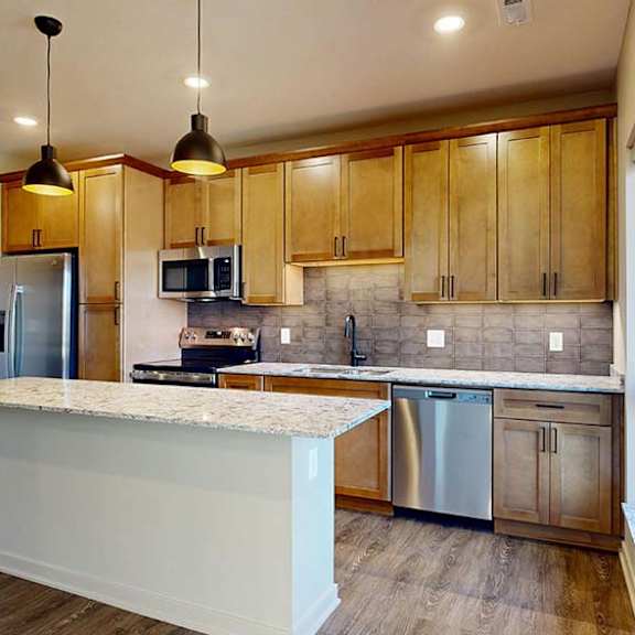 Thumbnail 24 of 36 Modern apartment kitchen with a large island, wood cabinetry, and stainless steel appliances.