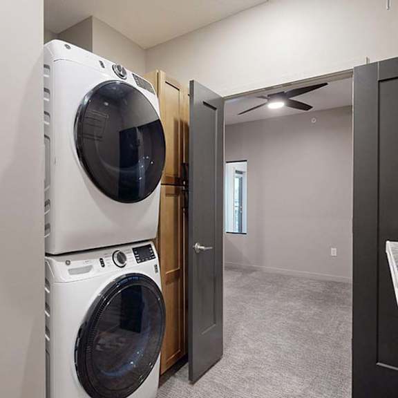 Thumbnail 30 of 36 Apartment laundry closet with a stacked washer and dryer and wire shelving.