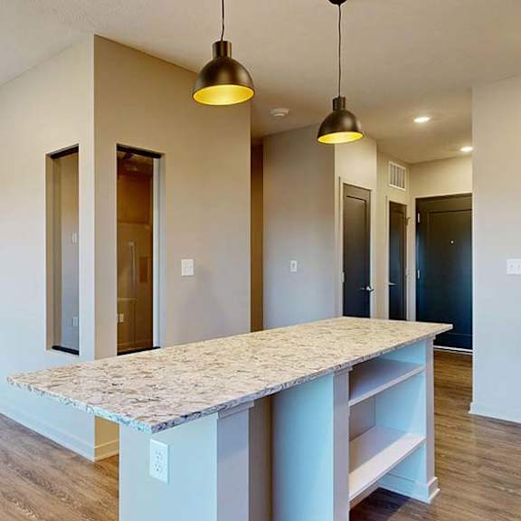 Thumbnail 26 of 36 Open apartment kitchen with a large island, pendant lighting, and wood-style flooring.