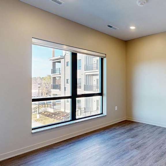 Thumbnail 27 of 36 Bright apartment room with a large window, wood-style flooring, and natural light.