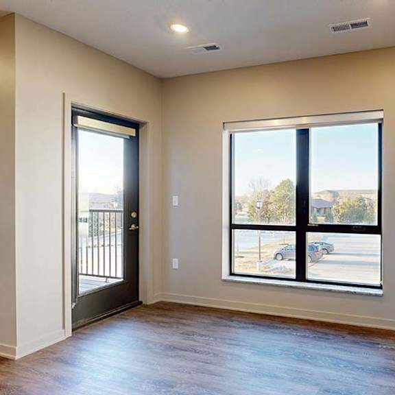Thumbnail 28 of 36 Bright apartment living area with wood-style flooring, large windows, and a door leading to a private balcony.