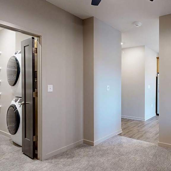 Thumbnail 33 of 36 Apartment bedroom with carpeted flooring, a large window, and a laundry closet with a stacked washer and dryer.