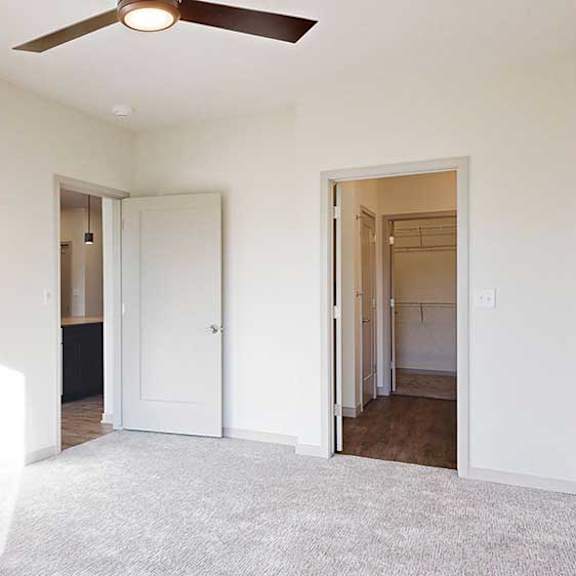 Thumbnail 17 of 30 a bedroom with carpeted flooring, a ceiling fan, and an attached bathroom with walk-in closet