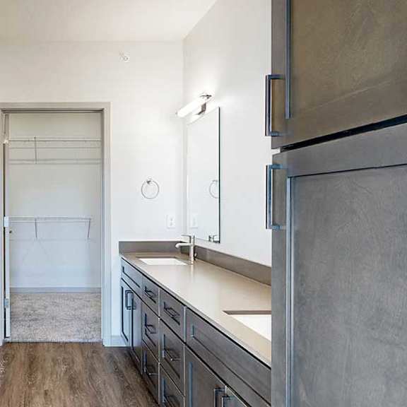 Thumbnail 18 of 30 a bathroom with a double vanity sink, two mirrors, a tall storage cabinet, and a walk-in closet at the end