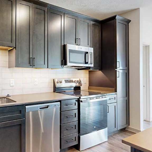 Thumbnail 7 of 30 a modern kitchen with dark wooden cabinets, quartz countertops, a tile backsplash, and stainless steel appliances