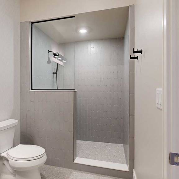 Thumbnail 10 of 46 A tiled walk-in shower with a half wall, glass window, and a shower head with detached sprayer.