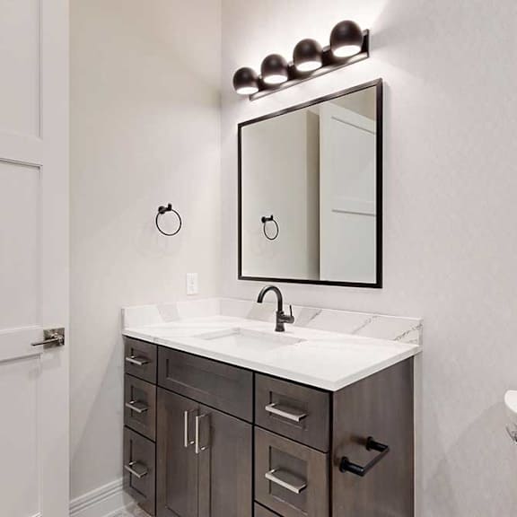 Thumbnail 8 of 46 A bathroom with a dark wood and light quartz vanity sink, with a framed mirror and overhead lighting.