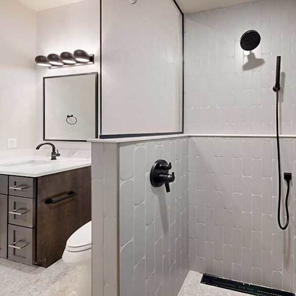 Thumbnail 11 of 46 A tiled walk-in shower with a half wall, glass window, and a shower head with detached sprayer.