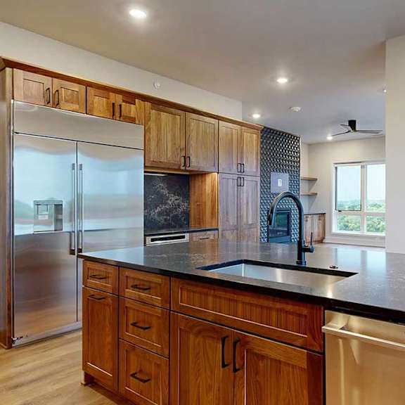 Thumbnail 20 of 46 A gourmet kitchen with an oversized island, oak wooden cabinetry, stainless steel appliances, quartz countertops, a range hood, and a tile backsplash.