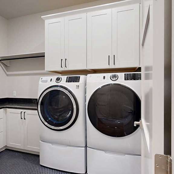 Thumbnail 46 of 46 A laundry room with a full-sized front-loading washer and dryer with overhead cabinetry for storage, and a utility sink with quartz counters.