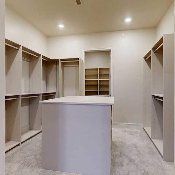 Thumbnail 36 of 46 A spacious boutique-style walk-in closet with built-in shelves, and a central cabinet.