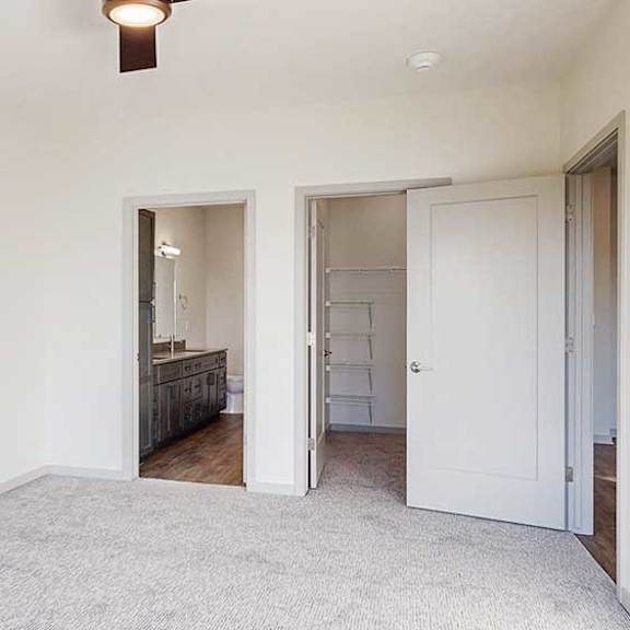Thumbnail 20 of 33 a bedroom with a carpeted floor, a ceiling fan, an attached bathroom, and a spacious walk-in closet