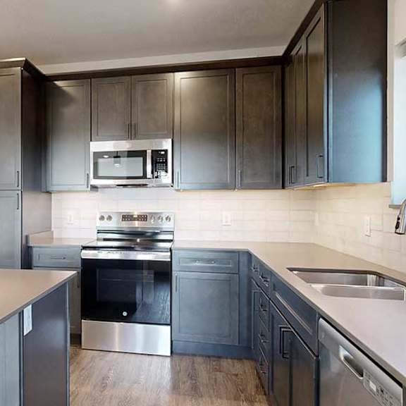 Thumbnail 5 of 33 a modern kitchen with dark wood cabinets, quartz countertops, a tile backsplash, and stainless steel appliances