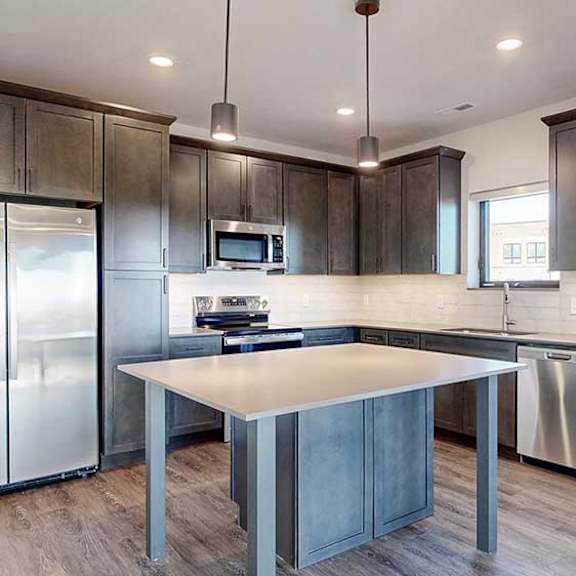 Thumbnail 4 of 33 a modern kitchen with dark wooden cabinets, quartz countertops, a tile backsplash, a large central island, and stainless steel appliances
