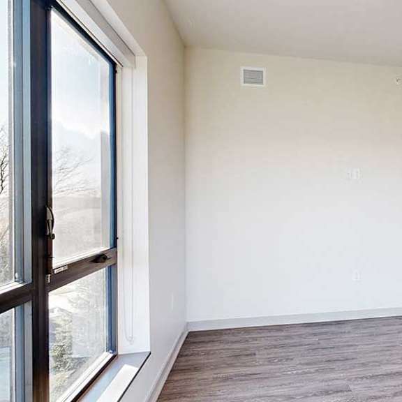 Thumbnail 16 of 33 a living room with a large window, hardwood flooring, and a door to a bedroom