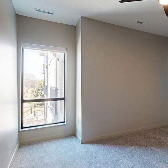 Thumbnail 44 of 46 Bright apartment bedroom with neutral carpeting, recessed lighting, and a large window that brings in natural light.