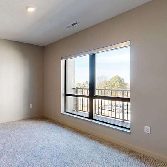 Thumbnail 39 of 46 Bright apartment bedroom with neutral carpeting, a large window overlooking the balcony, and soft natural light creating an open, airy feel.
