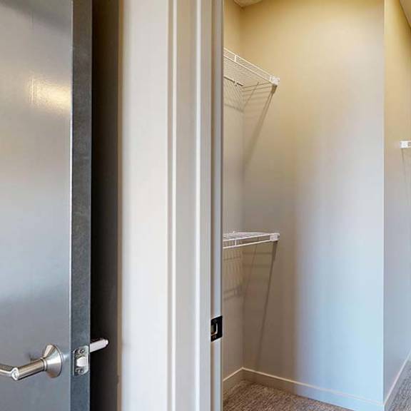 Thumbnail 40 of 46 Bright apartment walk-in closet with built-in wire shelving and an adjacent glass-enclosed shower, featuring neutral walls and wood-look flooring.