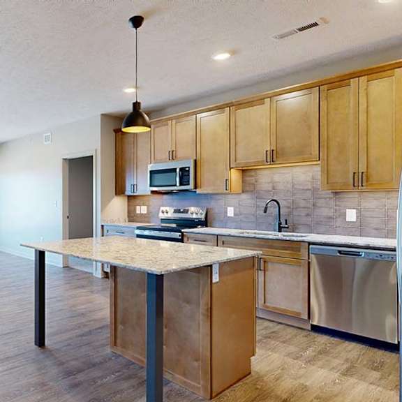 Thumbnail 31 of 46 Bright open-concept apartment kitchen and living area with a center island, wood cabinetry, stainless steel appliances, pendant lighting, and large windows.