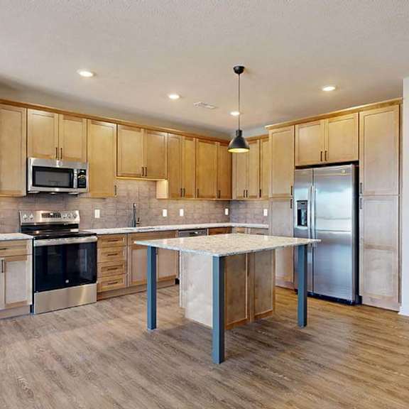 Thumbnail 33 of 46 Open-concept apartment kitchen with a center island, wood cabinetry, stainless steel appliances, and wood-look flooring flowing into the adjacent living area.