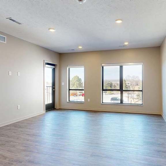 Thumbnail 34 of 46 Bright, open apartment living room with wood-look flooring, recessed lighting, large windows, and a sliding glass door that brings in natural light.