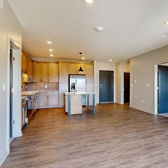 Thumbnail 35 of 46 Spacious open-concept apartment living area with wood-look flooring, recessed lighting, and a modern kitchen featuring a center island, wood cabinetry, and stainless steel appliances.