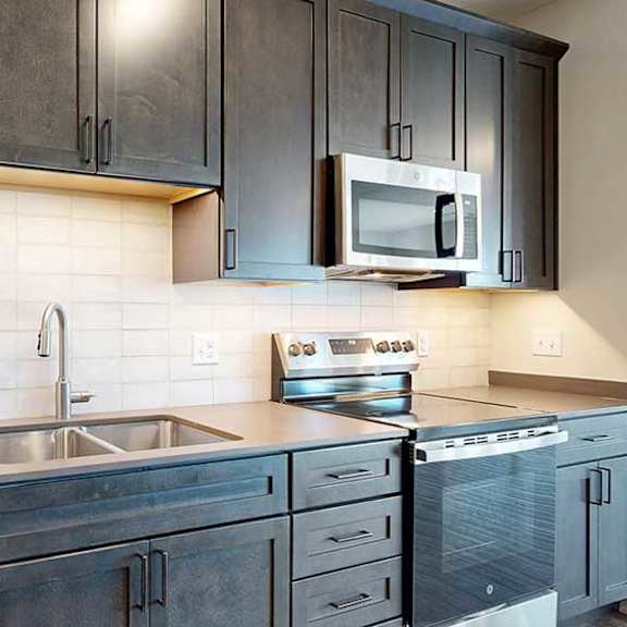 Thumbnail 6 of 30 a kitchen with dark cabinets, quartz cabinets, a tile backsplash, and stainless steel appliances