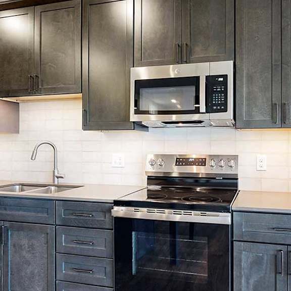 Thumbnail 5 of 30 a modern kitchen with dark cabinets, a tile backsplash, quartz countertops, and stainless steel appliances