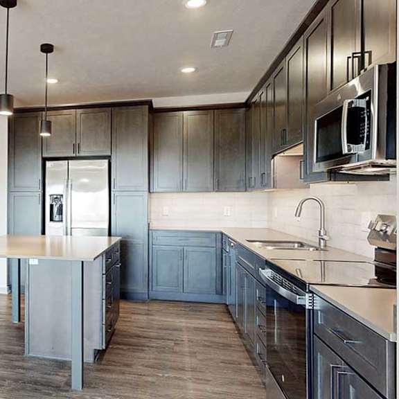 Thumbnail 3 of 30 a grey front door next to a modern kitchen with dark cabinets, a central table island, and quartz countertops