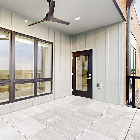 Thumbnail 15 of 41 An oversized balcony with a floor-to-ceiling window to the living room, stone tile flooring, a ceiling fan, and a windowed door to the living room.