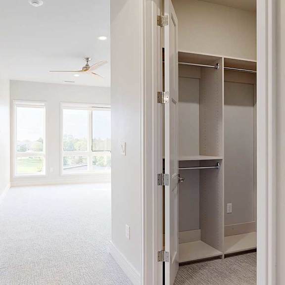 Thumbnail 20 of 41 A carpeted with floor-to-ceiling windows, a ceiling fan, and a walk-in closet with built-in wooden shelving.