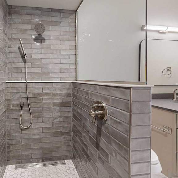 Thumbnail 27 of 41 A tiled walk-in shower with a half wall, glass window, and a shower head with detached sprayer.