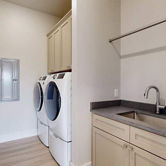 Thumbnail 29 of 41 A laundry room with a full-sized front-loading washer and dryer with overhead cabinetry for storage, and a utility sink with quartz counters.