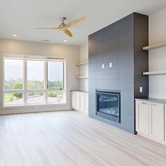 Thumbnail 18 of 41 A modern living room with a fire place in a floor-to-ceiling mantel, built-in cabinetry, floor-to-ceiling windows, hardwood-style flooring, and a ceiling fan.