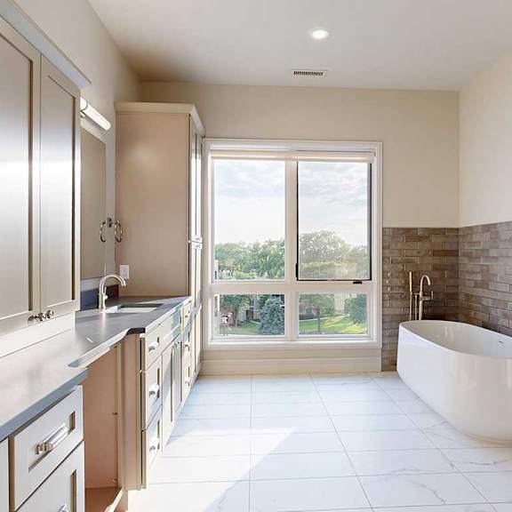 Thumbnail 33 of 41 A spacious ensuite bathroom with a double vanity sink, floor-to-ceiling window, soaking tub, and tiled flooring.