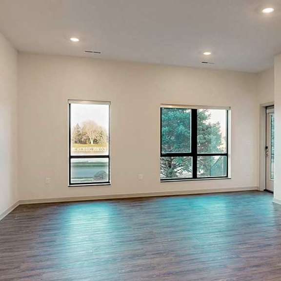 Thumbnail 10 of 26 a large living room with hardwood floors, two windows, and a door leading out to the patio