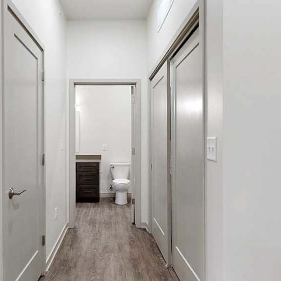 Thumbnail 23 of 25 a hallway with a door open to the bathroom, a closed entryway closet, and closed laundry room